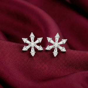 Snowflake-shaped silver earrings on a burgundy fabric background